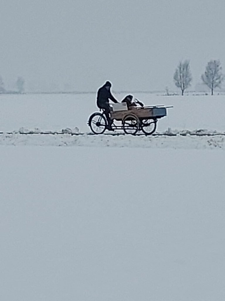 Een bakfiets rijdt door het besneeuwde Friese landschap